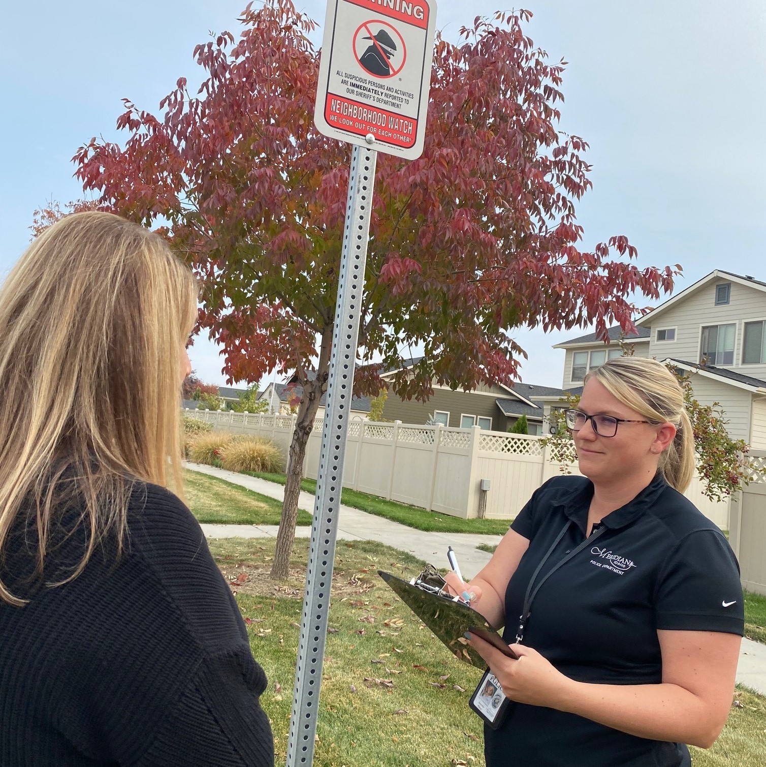Crime Prevention Specialist is in front of a Neighborhood Watch sign while writing on a clip board.
